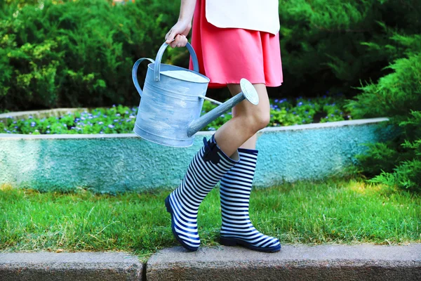 Jeune femme en bottes en caoutchouc tenant arrosoir, en plein air — Photo