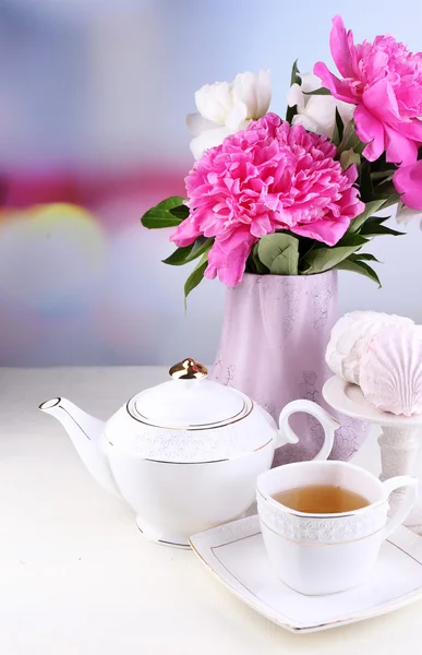 Cam vazo içinde sunulan güzel peonies, çay Kupası ve hatmi, masada açık renkli üzerinde kompozisyon