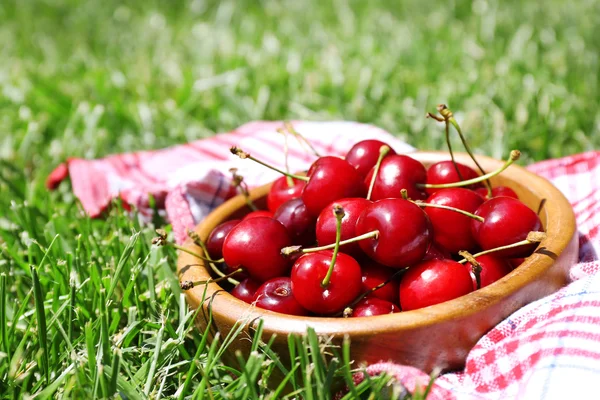 Sweet ripe cherries in wooden bowl, on napkin, on green grass background — Stock Photo, Image