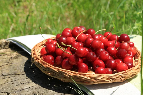 Sweet cherries on wicker stand with napkin on glade — Stock Photo, Image