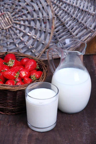 Mogna söta jordgubbar i rotting korg och kanna mjölk på färg trä bakgrund — 图库照片