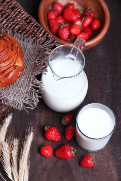 Fraises sucrées mûres dans un bol et une cruche en bois avec du lait sur fond en bois de couleur — Photo