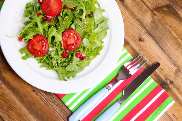 Salade verte à base de roquette, tomates et sésame sur assiette, sur fond de bois — Photo