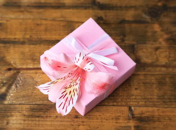 Presente rosa com arco e flor na mesa de madeira close-up — Fotografia de Stock