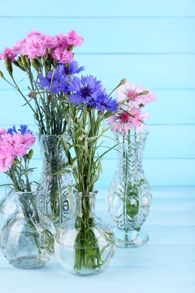 Schöne Sommerblumen in Vasen auf blauem Holzgrund — Stockfoto