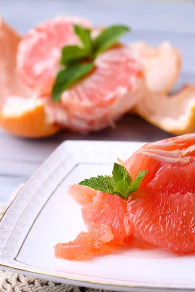 Reife geschälte Grapefruits auf Teller, auf farbigem Holztisch, auf hellem Hintergrund — Stockfoto
