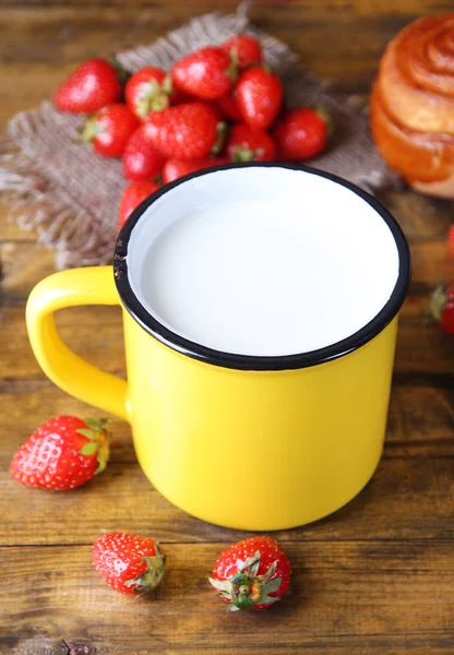 Ripe sweet strawberries, fresh bun and mug with milk on color wooden background — Stock Photo, Image