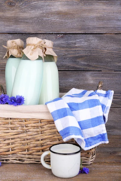 Flaschen Milch und Kornblumen in Weidenkorb auf hölzernem Hintergrund — Stockfoto