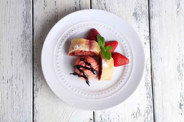 Вкусный домашний штрудель с мороженым, свежей клубникой и мятными листьями на тарелке, на деревянном фоне — стоковое фото