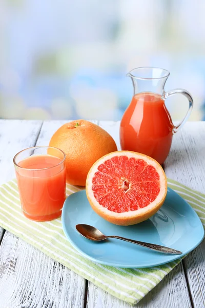 Hälften av grapefrukt, Glaskanna med färsk juice och sked på plattan på ljus bakgrund — Stockfoto