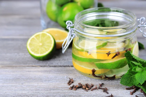 Limes sottaceto e chiodi di garofano in vaso di vetro, su tavolo di legno, su sfondo brillante — Foto Stock