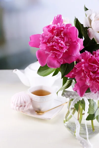 Composición de hermosas peonías en jarrón, té en taza y malvavisco, sobre mesa, sobre fondo claro — Foto de Stock