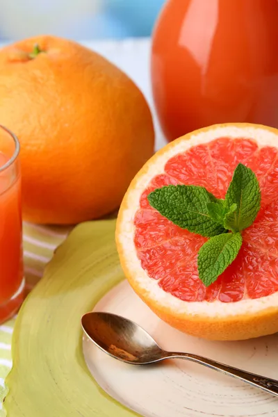 Hälfte Grapefruit, Glaskrug mit frischem Saft und Löffel auf Teller auf hellem Hintergrund — Stockfoto