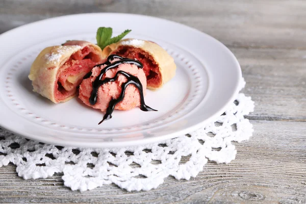 Strudel maison savoureux avec glace, fraise fraîche et feuilles de menthe sur assiette, sur fond de bois — Photo
