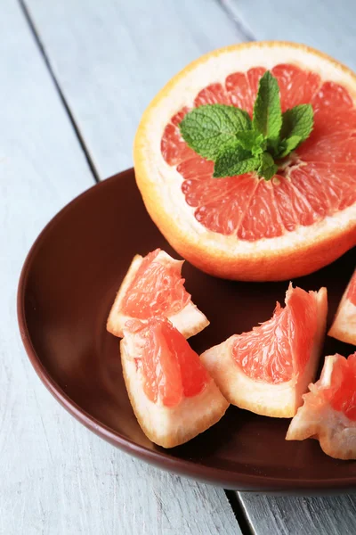 Ripe grapefruits on plate on color wooden background — Stock Photo, Image