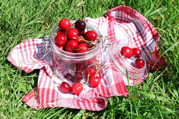 Cerises mûres douces dans un bocal en verre, sur une serviette, sur un fond d'herbe verte — Photo