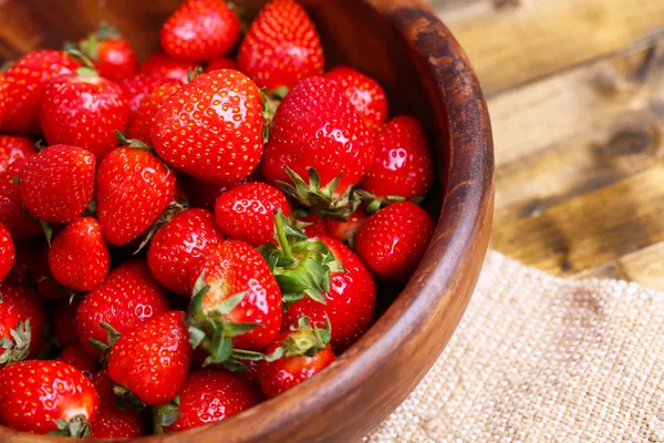 Reife süße Erdbeeren in Holzschale auf farbigem Holzhintergrund — Stockfoto