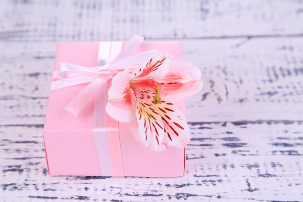 Ροζ δώρο με το τόξο και το λουλούδι στο ξύλινο τραπέζι close-up — Φωτογραφία Αρχείου