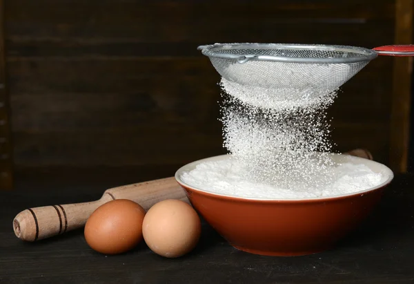 Sifting flour into bowl on table on wooden background — Stock Photo, Image