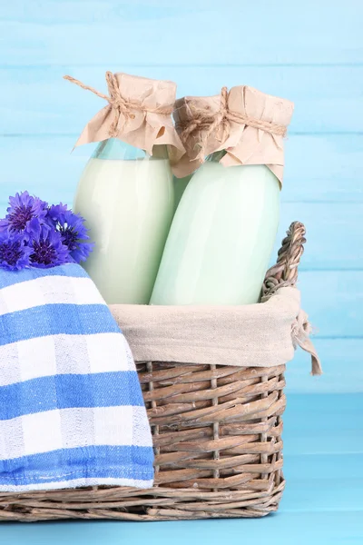 Бутылки молока и васильков в плетеной корзине на деревянном фоне — стоковое фото