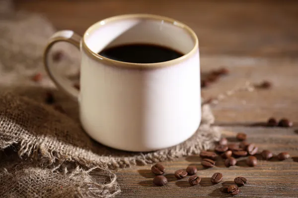 Copo com café quente e grãos de café torrados em fundo de mesa de madeira — Fotografia de Stock