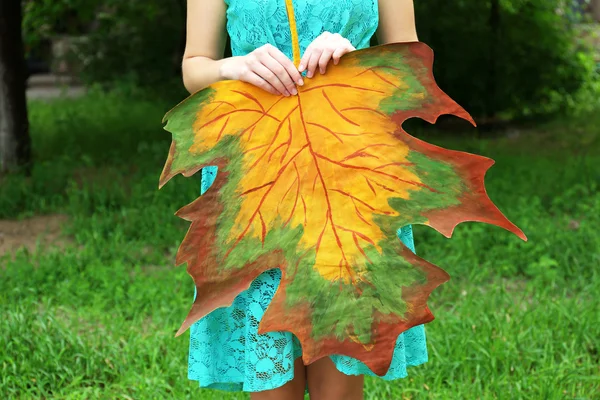 Girl holding decorative maple leaf in park — Stock Photo, Image