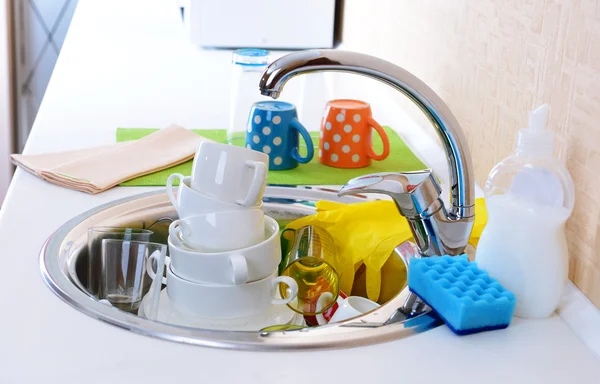 Stack of dishes soaking in kitchen sink — Stock Photo, Image