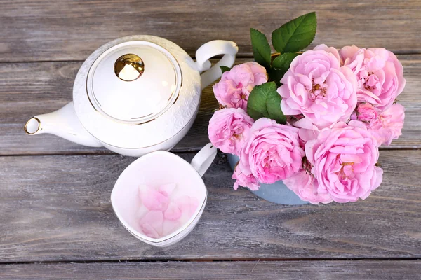 Frühstückstee mit Teekanne mit frischen rosa Gartenrosen auf farbigem Holzhintergrund — Stockfoto