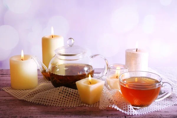 Σύνθεση με το τσάι στο φλιτζάνι και τσαγιέρα και κεριά στο τραπέζι, επάνω ελαφρύς υπόβαθρο — Φωτογραφία Αρχείου