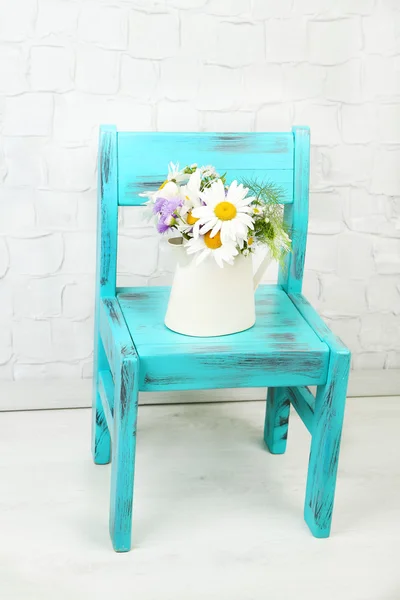 Bouquet of colorful flowers in decorative jug, on chair, on home interior background — Stock Photo, Image