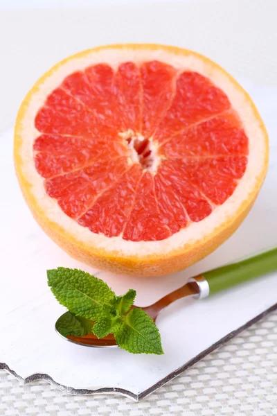 Mitad de pomelo y cuchara sobre tabla de madera sobre fondo claro — Foto de Stock