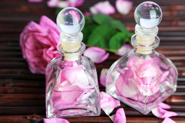 Óleo de rosa em garrafas no fundo da esteira de bambu — Fotografia de Stock
