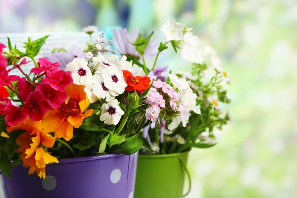 Bukett av färgglada blommor i dekorativa hinkar, på stol, på ljus bakgrund — Stockfoto