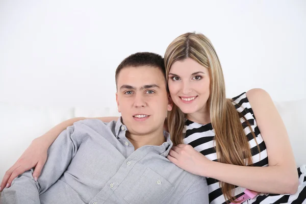 Liebendes Paar auf Sofa sitzend, auf hellem Hintergrund — Stockfoto