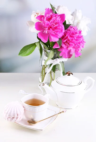 Composición de hermosas peonías en jarrón, té en taza y malvavisco, sobre mesa, sobre fondo claro —  Fotos de Stock