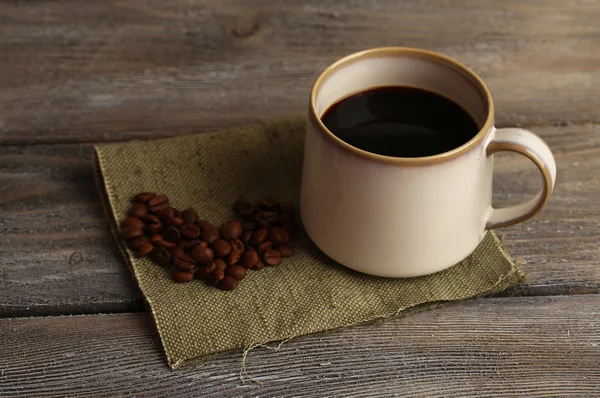 Cup with hot coffee and roasted coffee grains on napkin, on wooden table background — Stock Photo, Image