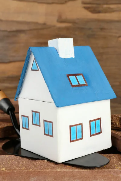 Wooden toy house on trowel and tiles on wooden background, close up — Stock Photo, Image