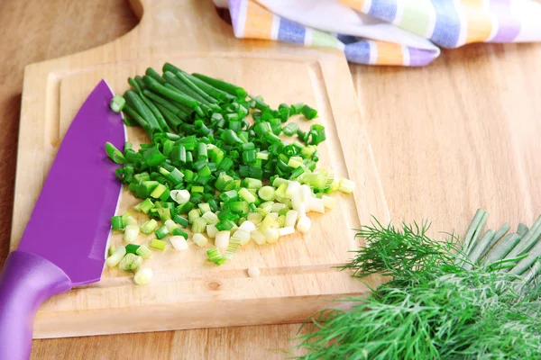Cebolla verde picada con cuchillo en tabla de cortar sobre mesa de madera —  Fotos de Stock