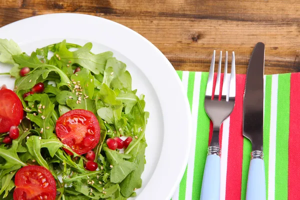 Zelený salát s rukolou, rajčaty a sezam na desku, na dřevěné pozadí — Stock fotografie
