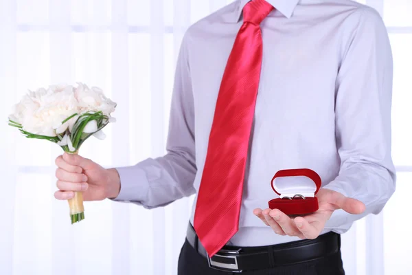 Man holding wedding bouquet and rings on light background — Stock Photo, Image