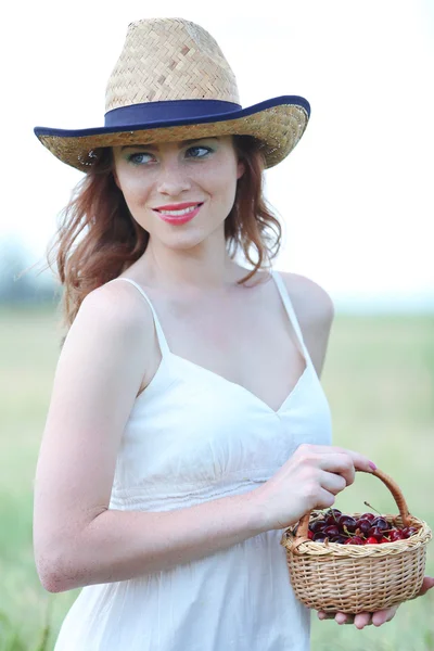 Piękna młoda kobieta trzyma Wiklinowy kosz z wiśniami w dziedzinie — Zdjęcie stockowe