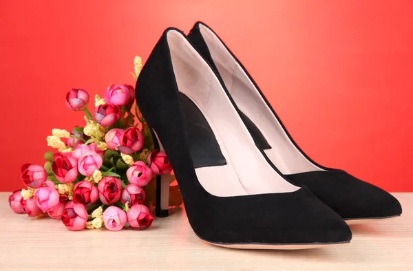 Vackra svarta kvinnliga skor och blommor på röd bakgrund — Stockfoto