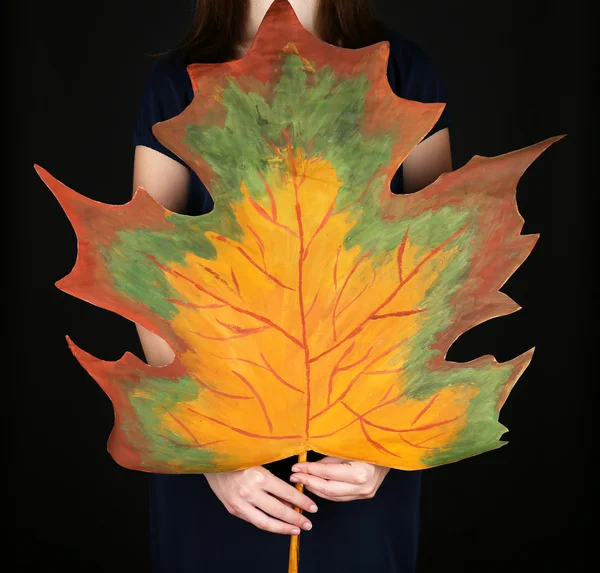 Girl holding decorative maple leaf on black background — Stock Photo, Image