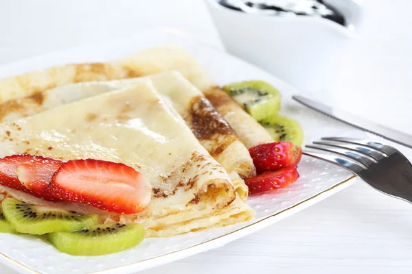 Heerlijke pannenkoeken met aardbeien en chocolade op plaat op tafel — Stockfoto