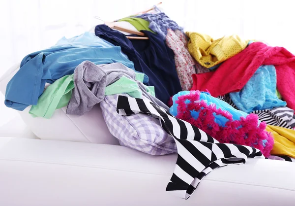 Грязная разноцветная одежда на диване на светлом фоне — стоковое фото