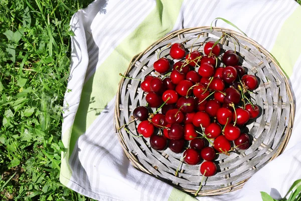 Sweet ripe cherries on wicker mat, on green grass background — Stock Photo, Image