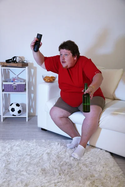 Lazy overweight male sitting on couch and watching television — Stock Photo, Image