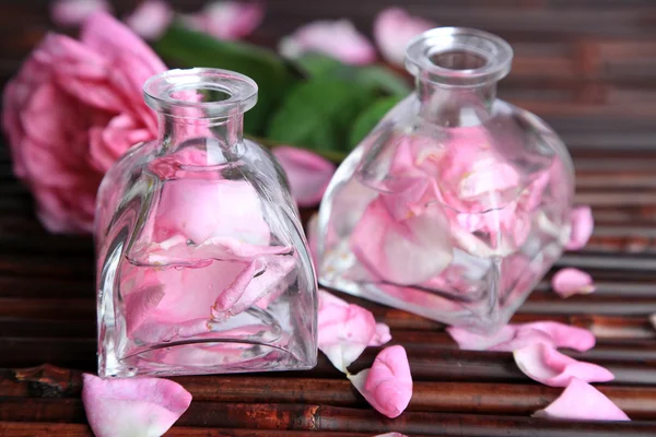 Olio di rosa in bottiglie su sfondo tappetino di bambù — Foto Stock