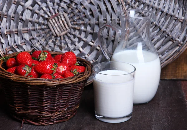 Ripe sweet strawberries in wicker basket and jug with milk on color wooden background — Stock Photo, Image