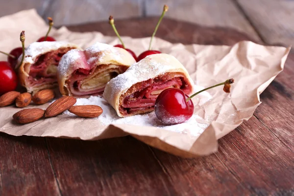 Gustoso strudel fatto in casa e dolce ciliegia fresca su tovagliolo di carta, su sfondo tavolo di legno — Foto Stock